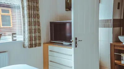 a bathroom with a tv on a dresser with a window at Bonnie Banks Lodge Ardlui in Ardlui