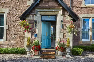 a blue door on a brick house with flowers at Merlindale in Crieff