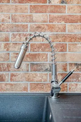 a kitchen sink with a hose attached to a brick wall at Central Bright 3 Bed Flat with Pool & Parking in Edinburgh