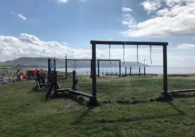 a group of swings in a field near the ocean at Fisher Holiday Cottage Ayrshire in Girvan