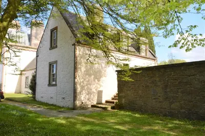 a white house with a brick wall and a tree at Rhoda`s Cottage in Creggans