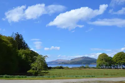 a field with a fence and a lake and mountains at Rhoda`s Cottage in Creggans