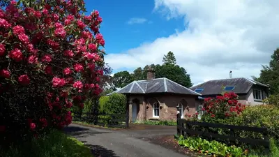 a house with a fence and flowers in front of it at North Lodge of Orchil in Braco