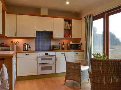 a kitchen with white cabinets and a table and chairs at Tigh An Aighear in Arduaine