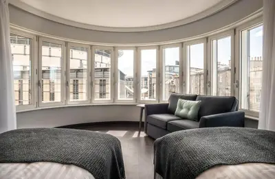 a room with two beds and a couch and windows at Point A Hotel Edinburgh Haymarket in Edinburgh