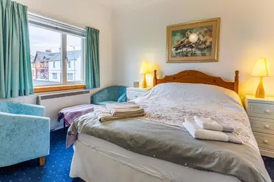 a bedroom with a bed and a chair and a window at Beach Front Flat, Brodick in Brodick