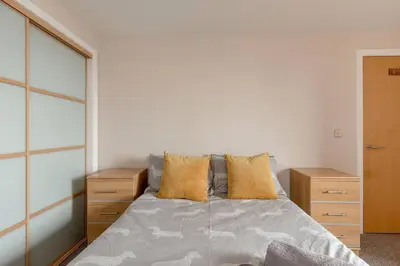 a bedroom with a bed and some wooden dressers at Modern Riverfront Apt. 10 mins from Hydro/SECC in Glasgow