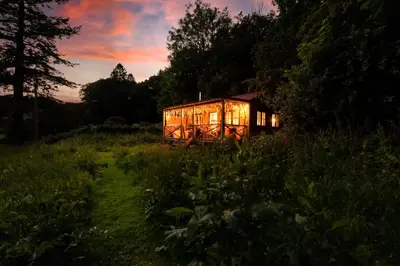 a house in a field with lights on at Luxury Off-Grid Cabin with Outdoor Bath in Scotland in Clachan of Campsie