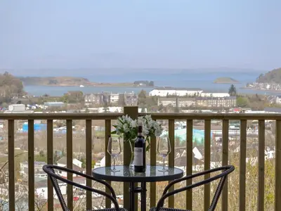 a table with wine glasses and flowers on a balcony at Sealladh Alainn in Oban