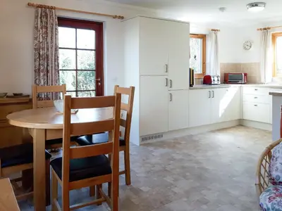 a kitchen with white cabinets and a table and chairs at Lismore Cottage in North Ballachulish