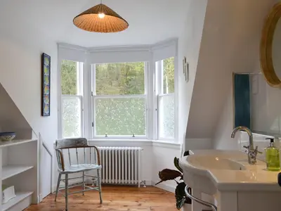 a bathroom with a sink and a window and a chair at Fircliff - The House On Bute in Port Bannatyne