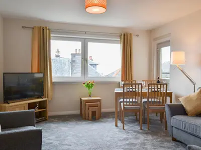 a living room with a table and chairs and a television at Finlaggan Apartment in Oban