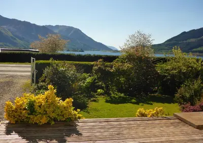 a wooden walkway with flowers and a view of the water at Camus Bhan in Ballachulish