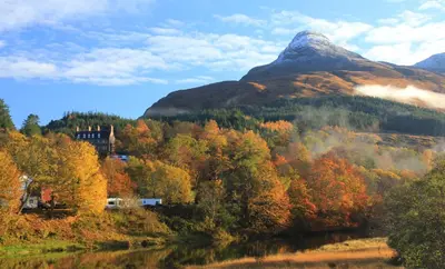 a mountain in the middle of a forest with a river at Camus Bhan in Ballachulish