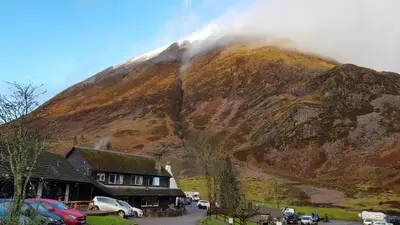 a mountain with cars parked in front of a building at Clachaig Inn in Ballachulish