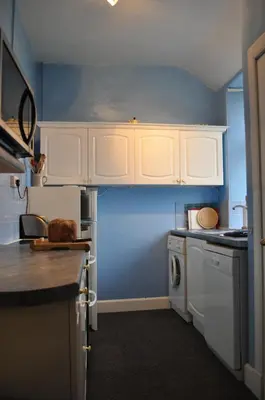 a kitchen with white cabinets and a blue wall at Auchmore Apartments in Killin