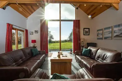 a living room with leather furniture and a large window at Powdermills B & B in Inveraray