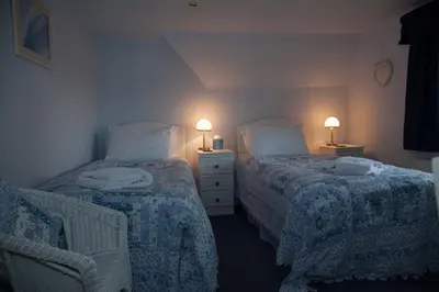 two beds in a room with two lamps and a chair at Dunchraigaig House in Kilmartin