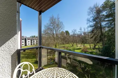 a balcony with two chairs and a view of a park at Gleneagles Apartment - Guthrie Court Gleneagles in Auchterarder
