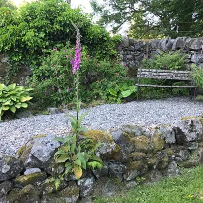 a stone wall with a bench in a garden at Mews Cottage Ardoch Lodge Strathyre in Strathyre