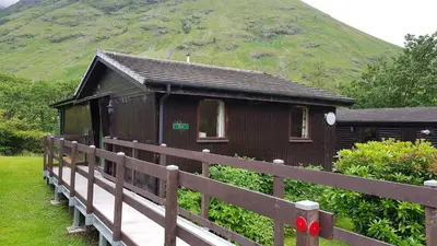 a small wooden cabin with a mountain in the background at Birch Chalet in Ballachulish