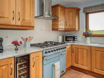 a kitchen with wooden cabinets and a blue stove top oven at Corsewall Castle Farm Lodges in Stranraer