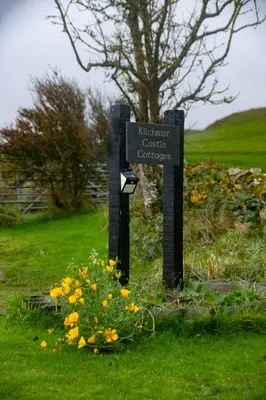 a sign in the grass next to some flowers at Kilchrist Castle Cottages in Campbeltown