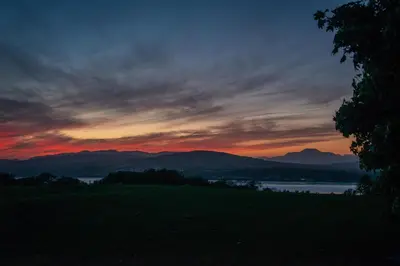 a sunset over a field with a lake and mountains at Super King Lodge-Sleeps 2-HotTub-Sea View in Langbank