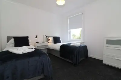 a white bedroom with two beds and a window at Signature - New View Place in Bellshill