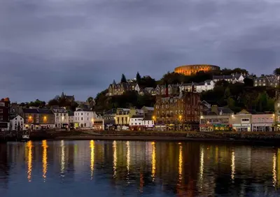a city lit up at night with buildings and the water at Panoramic Harbour View Apartment in Oban