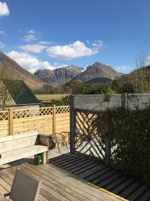 a wooden deck with a bench and mountains in the background at Hawthorn Cottage in Glencoe