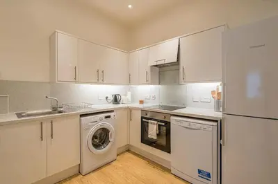 a kitchen with white cabinets and a washer and dryer at 2BR Grassmarket Apartment with Castle View in Edinburgh