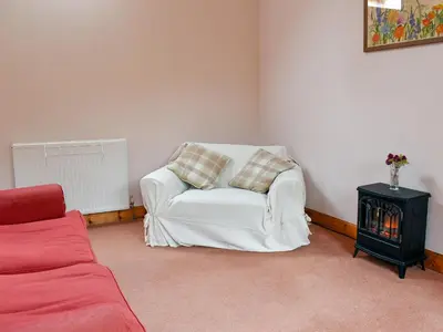 a living room with a white chair and a table at The Cottage At Cauldcoats in Linlithgow