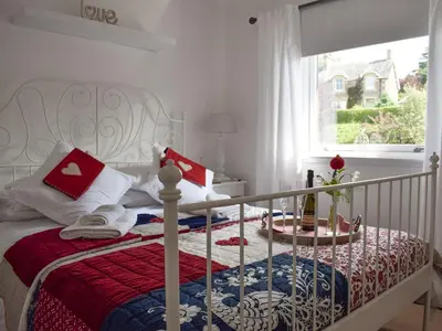 a white bed with a red and blue blanket and a window at Tree Tops in Crieff