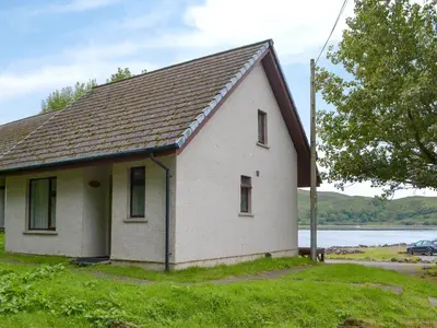 a small white house on the side of a lake at Puffin - Bach in Lerags