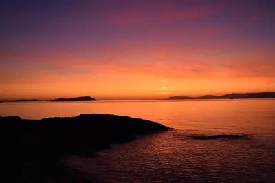 a sunset over the ocean with a rock in the water at Number 10, Isle of Luing in Cullipool