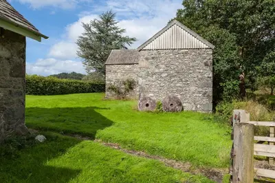 an old stone building with two objects in the grass at Enchanting,rustic, Dundurn Mill with stunning views and private river in Comrie