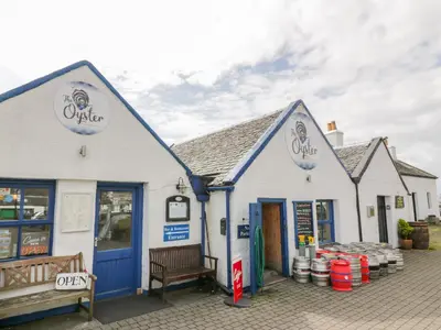 two white buildings with blue doors and a bench at Grebe Cottage in Oban