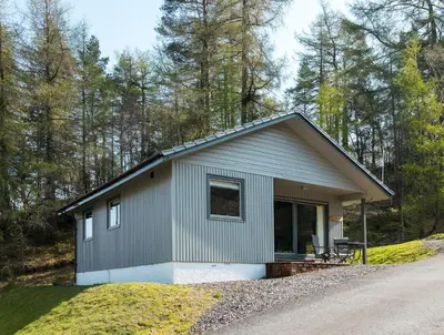 a small house on a hill next to a road at Deerstalker Lodge cozy lodge with wood burner in Crianlarich