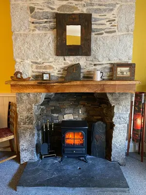 a stone fireplace with a wood stove in a room at Holly Cottage in Glencoe