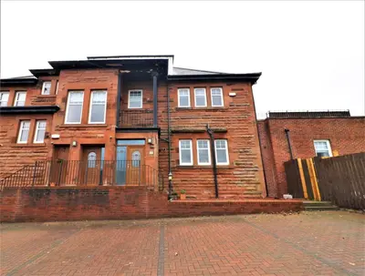 a brick building on a street with a fence at Signature - Greenlees Clubhouse in Glasgow