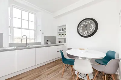 a kitchen with a table and chairs and a clock on the wall at Heart of Edinburgh City Centre 3 Bed Georgian Apt in Edinburgh