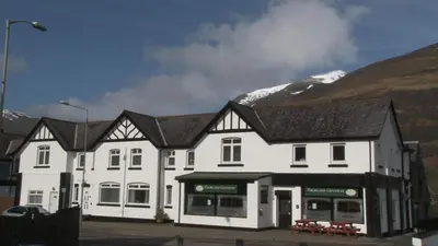 a large white building with a snow covered mountain behind it at Highland Getaway in Kinlochleven