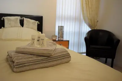 a bed with a pile of towels and a chair at Airdrie Apartments in Airdrie