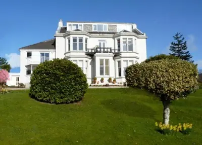 a large white house with two bushes in the yard at Kinneil Self Catering in Lamlash