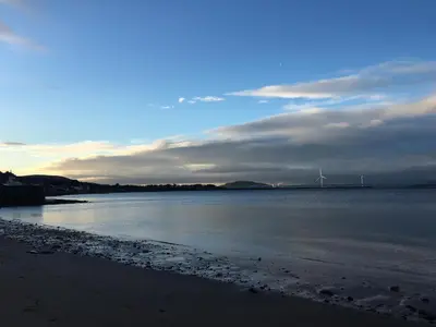 a view of a beach with a windmill in the distance at Beach House No1 With Amazing Sea Views And Direct Beach Access in Fairlie