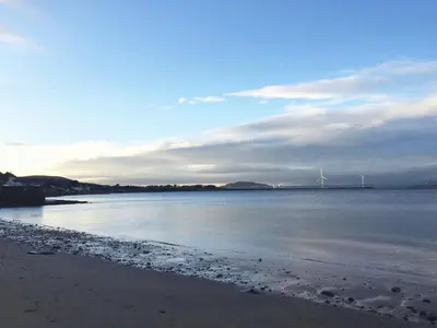 a view of a beach with a windmill in the distance at Beach House No1 With Amazing Sea Views And Direct Beach Access in Fairlie