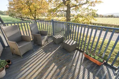 a porch with two chairs and a fence with a field at Dunroamin Apartment in Drymen