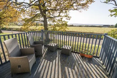 a deck with chairs and a fence and a field at Dunroamin Apartment in Drymen