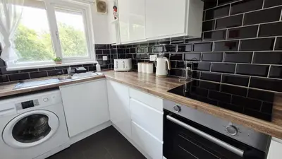 a kitchen with white cabinets and a washer and dryer at Levenhowe Holiday Apartment in Balloch